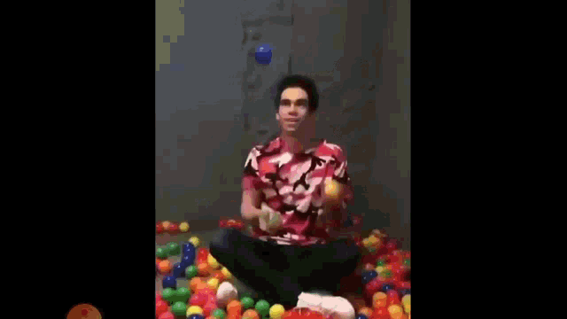 a man is sitting in a ball pit holding two balls in his hand .