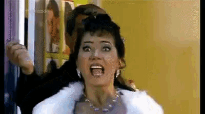 a woman in a fur coat is screaming while a man holds her hair in a room .