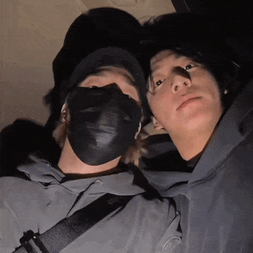 a man wearing a black mask stands next to another man wearing a hat
