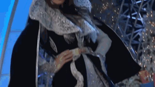 a woman in a black and white dress is standing on a stage with christmas lights in the background .