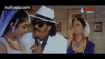 a man and two women are standing next to each other in a room . the man is wearing a hat and sunglasses .