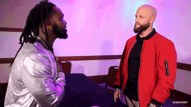 two men are standing next to each other in a room with purple lights behind them and one of the men is wearing a silver jacket