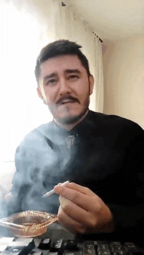 a man with a beard is smoking a cigarette in front of a keyboard