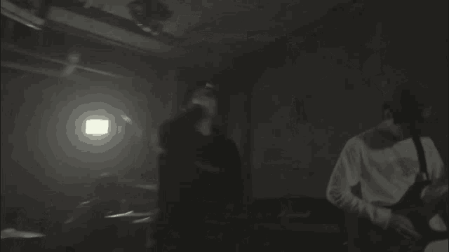 a man is singing into a microphone in a dark room while another man plays a guitar .