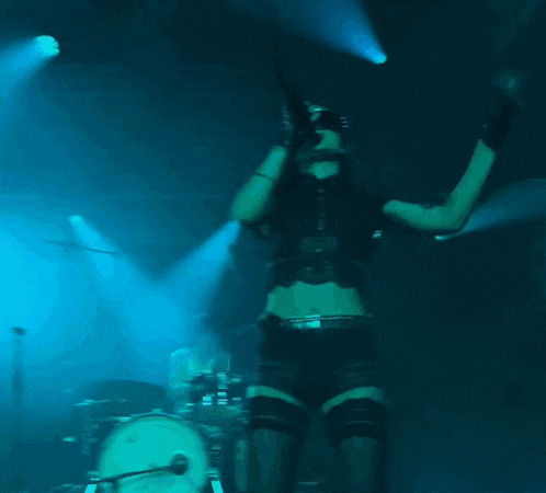 a woman singing into a microphone on a stage in front of a drum set