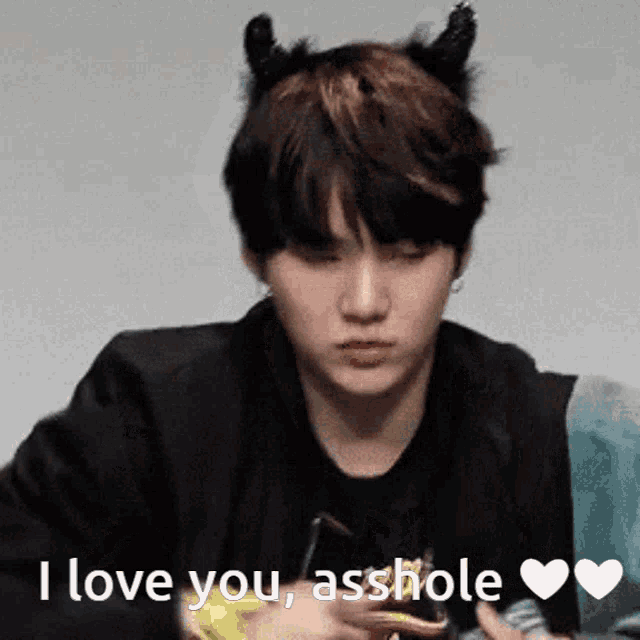 a young man with horns on his head is holding a cell phone and saying i love you asshole