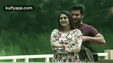 a man and a woman are standing next to each other with their arms crossed in a park .
