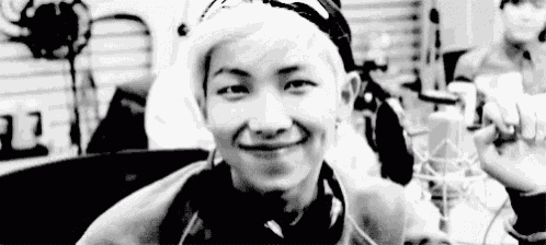 a black and white photo of a young man with white hair smiling in front of a microphone .