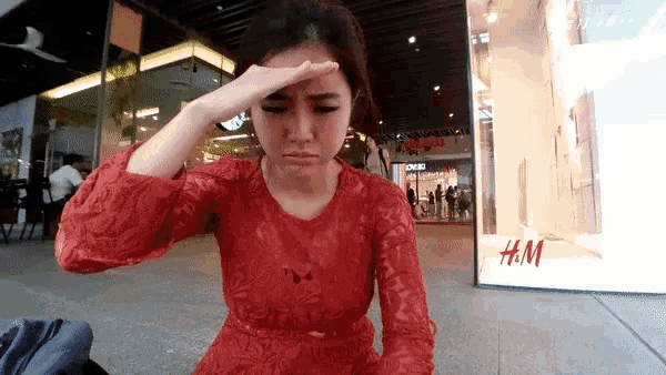 a woman in a red dress has her hand on her forehead in front of a store window that says h & m