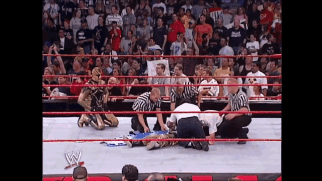 a wrestler is laying on the ground in a wrestling ring with a crowd watching .