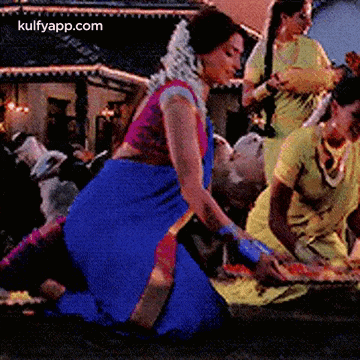 a woman in a blue saree is kneeling down in front of a man in a yellow dress .