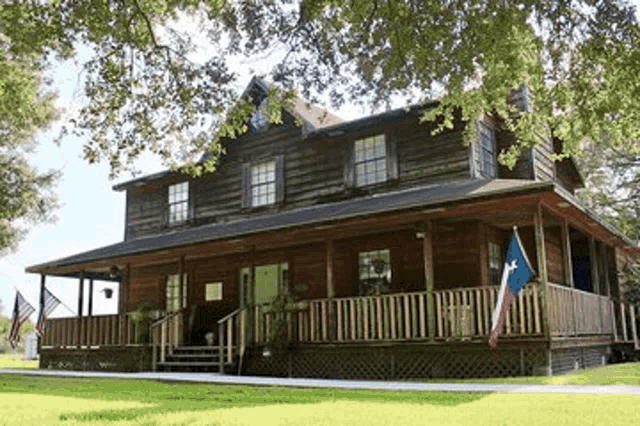 a large wooden house with a large porch and a texas flag on the porch .