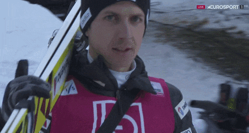 a man is carrying skis and wearing a vest that says eurosport 1