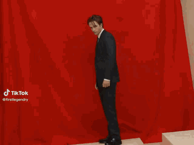 a man in a suit holds another man 's hand in front of a red background with a tiktok watermark