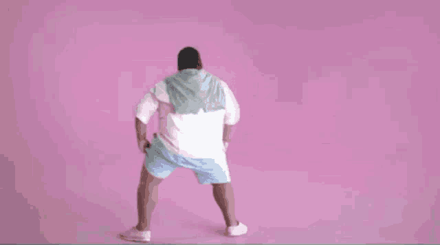 a man in a white shirt and blue shorts is dancing in front of a pink background .