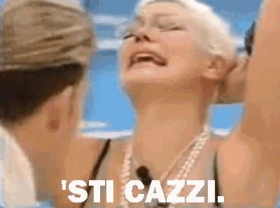 a woman with a pearl necklace says ' sti cazzi ' in front of a man kissing her on the cheek