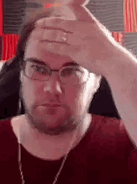 a man with glasses and a red shirt is holding his hand to his forehead