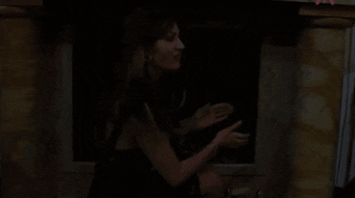 a woman in a black dress is standing in front of a fireplace in a dark room .