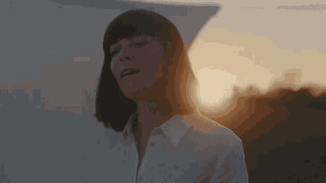 a woman in a white shirt is standing in a field at sunset .