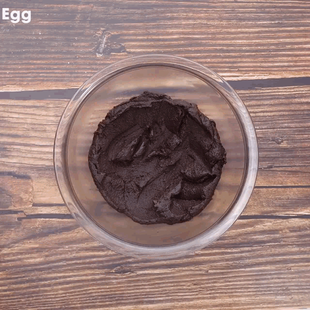 a glass bowl filled with a brown substance is on a wooden table with the word egg above it