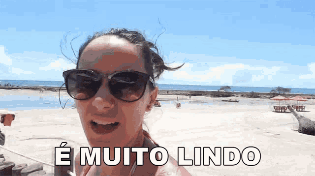 a woman wearing sunglasses is standing on a beach and says e muito lindo