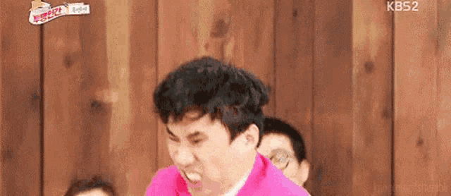 a man in a pink jacket is making a funny face while standing in front of a wooden wall .