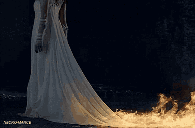 a woman in a white dress is standing in front of a large fire .