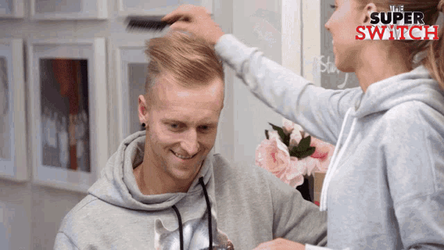 a woman brushes a man 's hair in front of a sign that reads the super switch