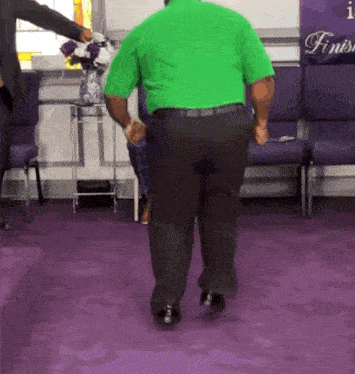 a man in a green shirt is dancing in a room with purple chairs