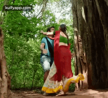 a man and a woman are dancing in the woods in front of a tree .