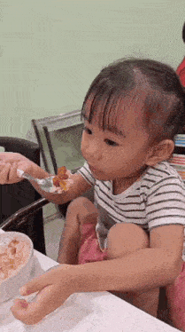 a little girl is eating food with a spoon .