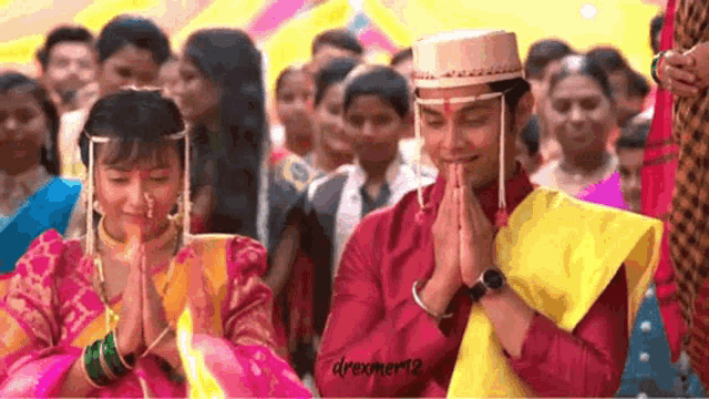 a bride and groom are praying together in front of a crowd of people .