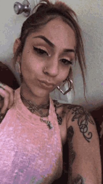 a woman wearing a pink top and earrings is making a funny face .