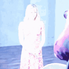 a woman in a pink dress is standing in front of a camera and smiling .