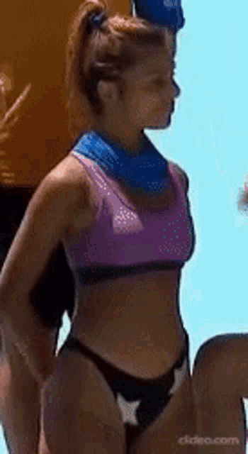 a woman in a purple bikini top and black bikini bottoms is standing next to a man .