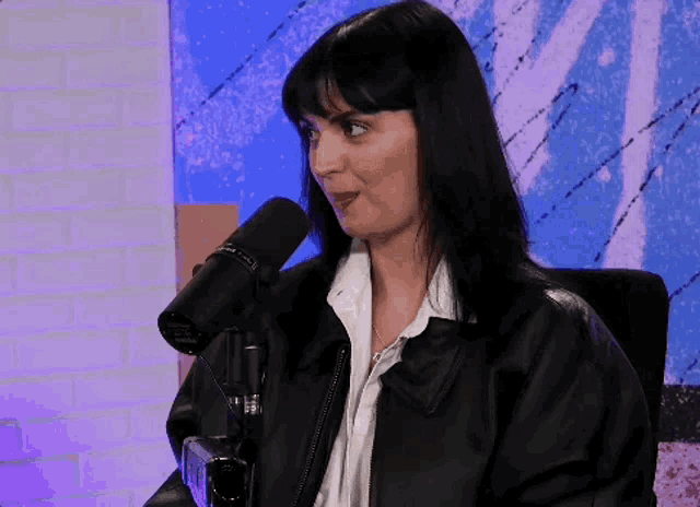 a woman in a leather jacket is sitting in front of a microphone and making a funny face .