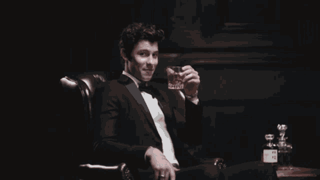 a man in a tuxedo is sitting in a chair with a glass of whiskey in his hand