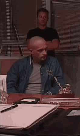 a man in a blue jacket is sitting at a desk with a pen in his hand