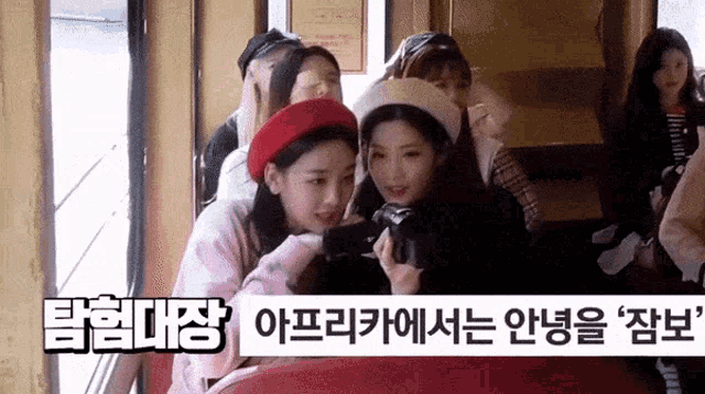 a group of young women are sitting on a train and one of them is holding a camera .