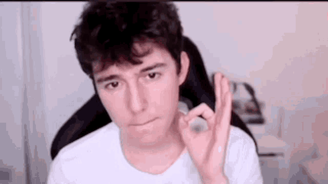 a young man is sitting in a chair and making an ok sign .