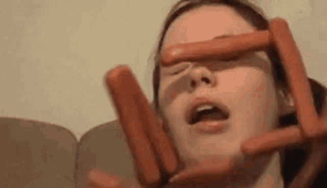 a woman is holding hot dogs to her face .