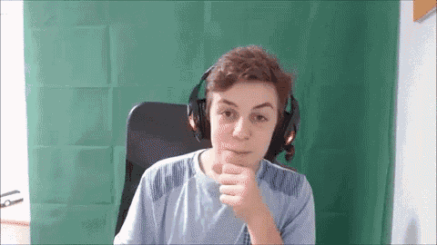 a young man wearing headphones is sitting in front of a green curtain and giving a thumbs up .