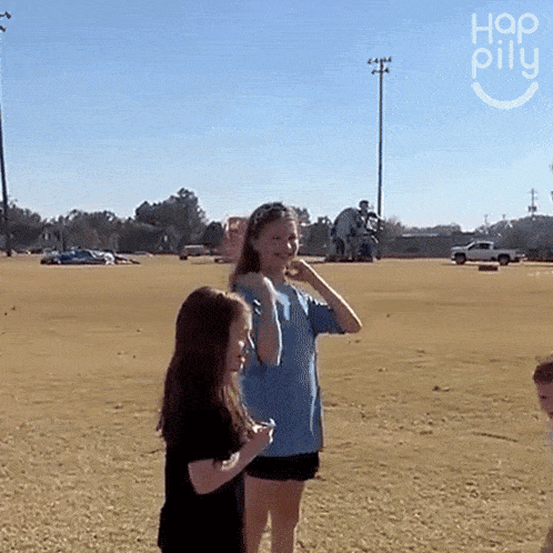 a girl in a blue shirt stands in a field next to another girl in a black shirt