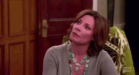 a woman is sitting in a chair wearing a turquoise necklace and a gray sweater .