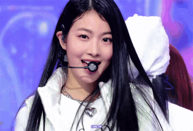 a girl with long black hair is wearing a white jacket and a necklace with a heart shaped pendant