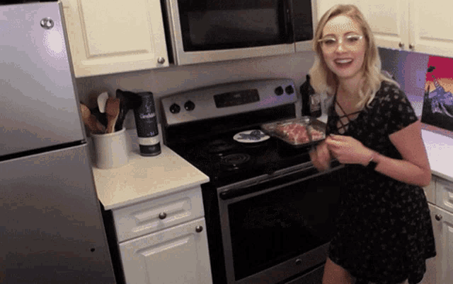 a woman stands in front of a stove in a kitchen holding a pan of meat