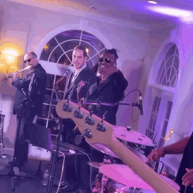 a group of men are playing instruments in a room with purple lighting