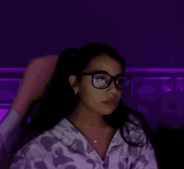 a woman wearing glasses and a hoodie is sitting in a chair .
