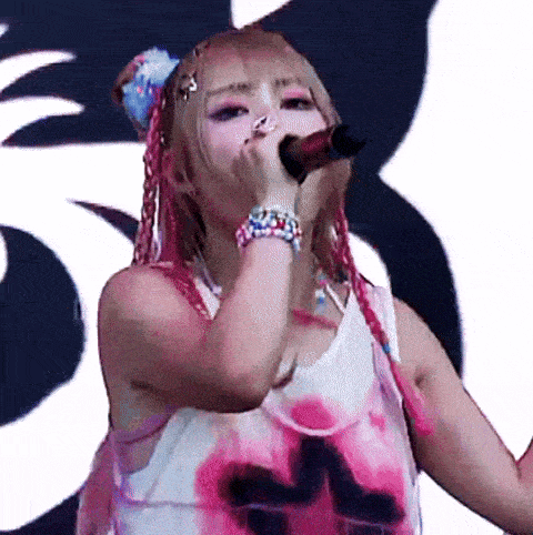a woman with pink hair is singing into a microphone while wearing a tank top with the letter m on it .