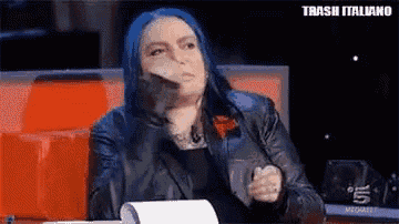 a woman with blue hair is sitting at a table with a piece of paper in her hand .